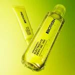 Flacone trasparente e tubo giallo Biotherm Aquasource+ Eau de Lait Demaquillante con gocce d’acqua visibili, su sfondo verde luminoso sfumato.