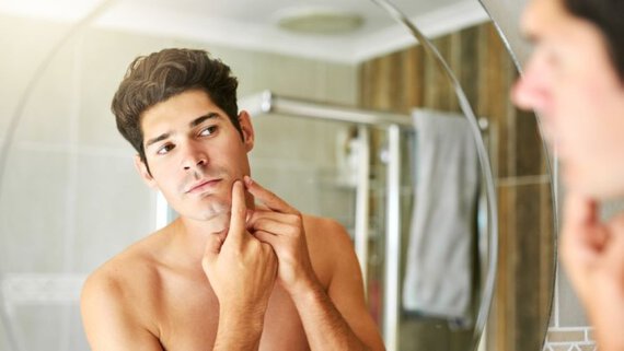 A man shaving his face while looking in the mirror.