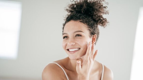 A woman happily applying facial cream, enhancing her skincare routine with a smile of contentment.
